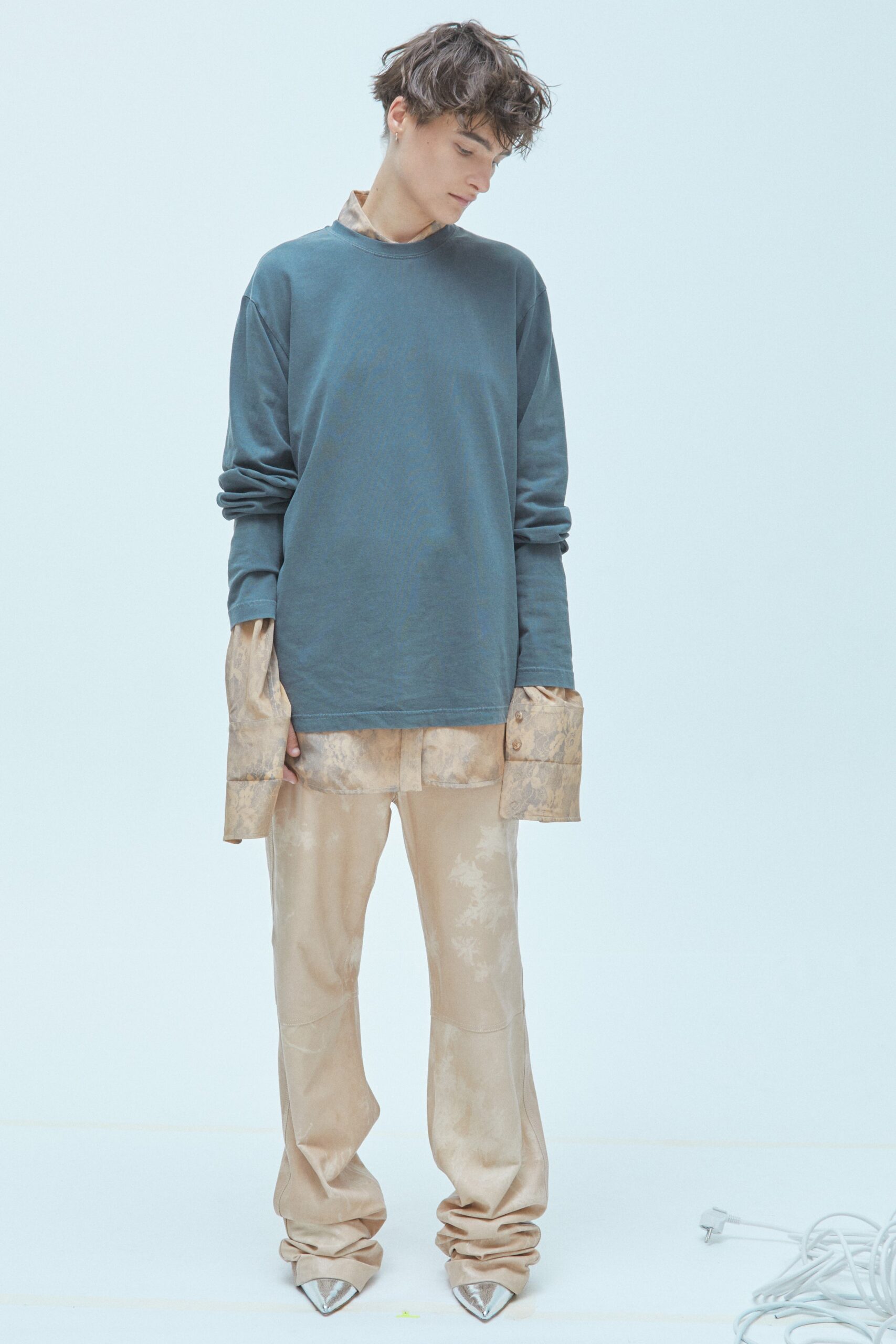 A relaxed blue long-sleeve top layered over a beige shirt paired with beige pants.