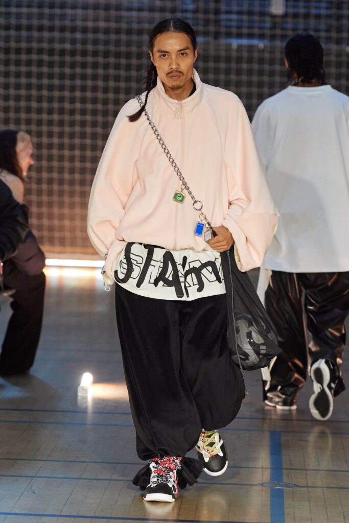 An oversized pink long-sleeve top with a printed design, paired with black pants.