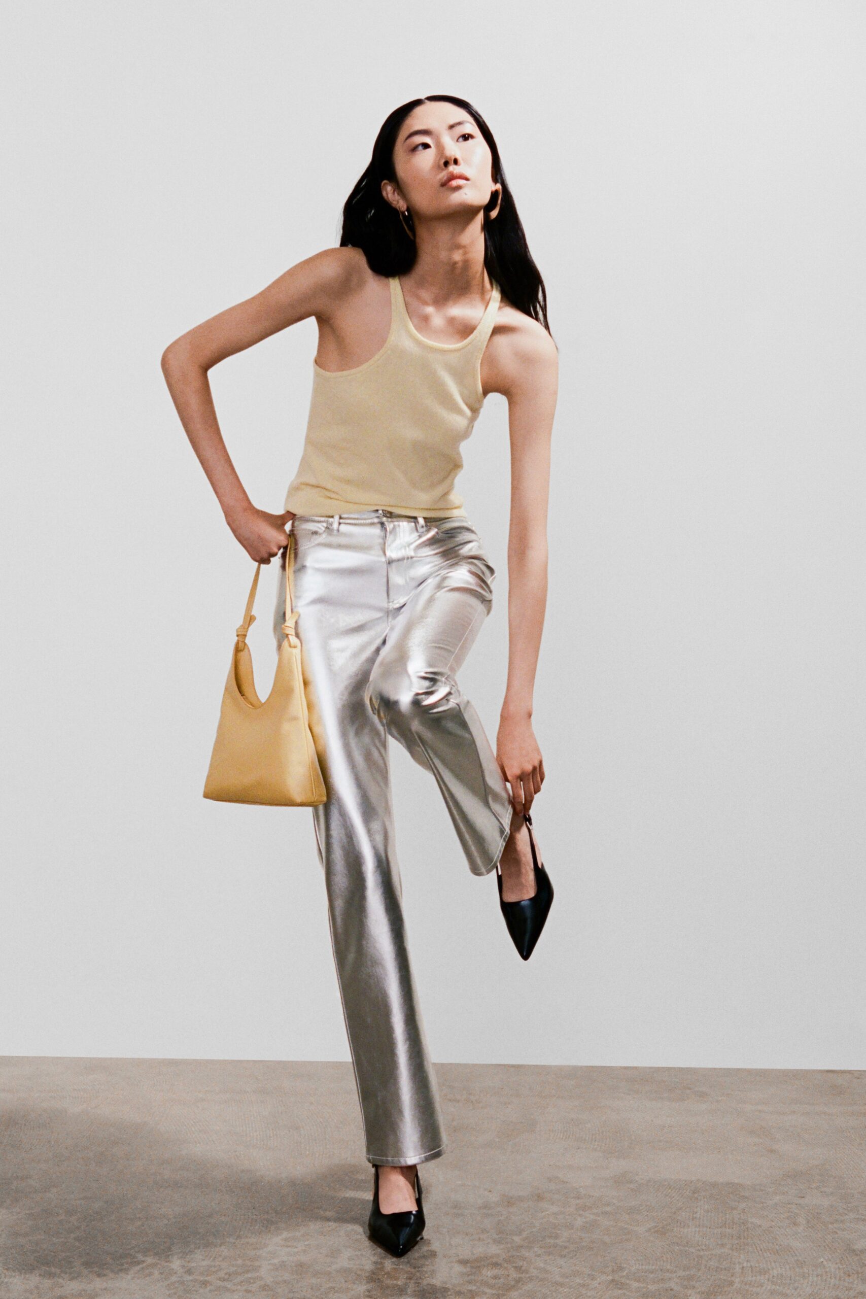A fitted beige sleeveless tank-top paired with high-waisted silver straight-leg pants.