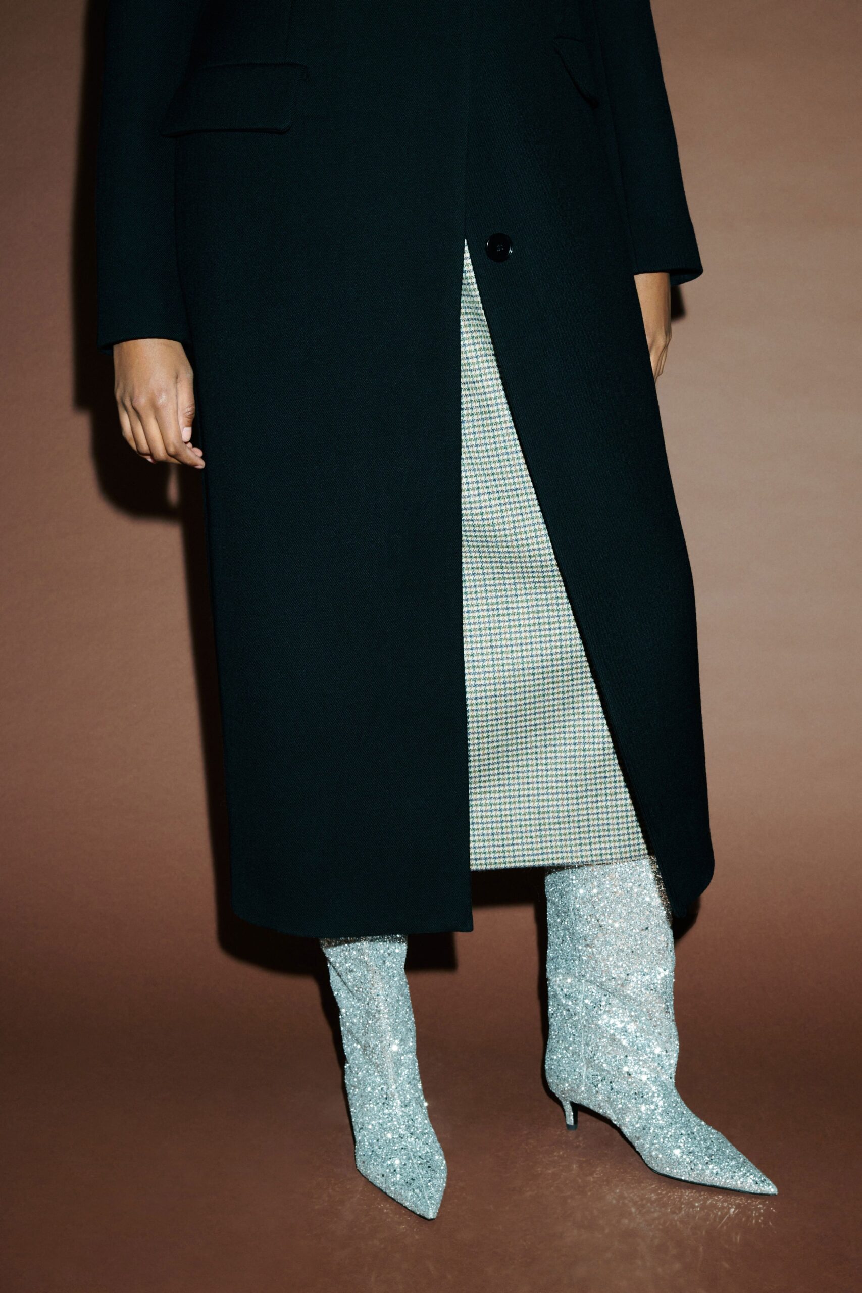 A fitted black wool coat paired with a gray checked skirt featuring an asymmetric design.