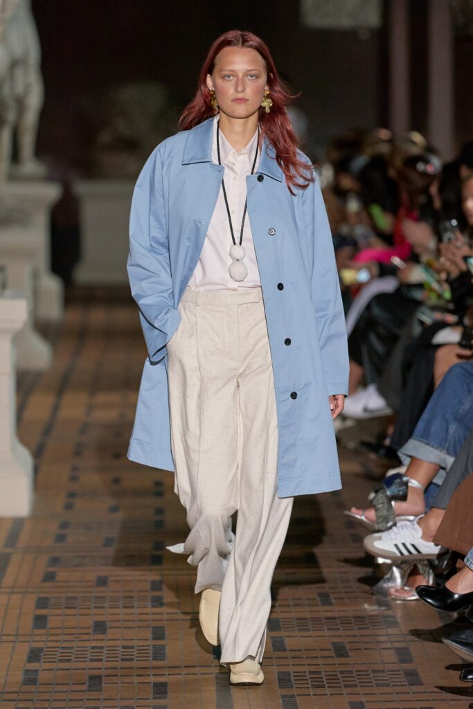 A relaxed blue cotton coat paired with straight-leg beige pants and a collared shirt.