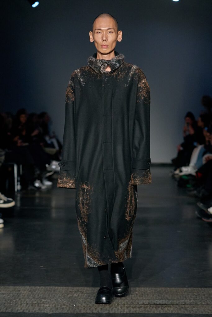 A relaxed black wool coat with long sleeves and an asymmetric design detail.
