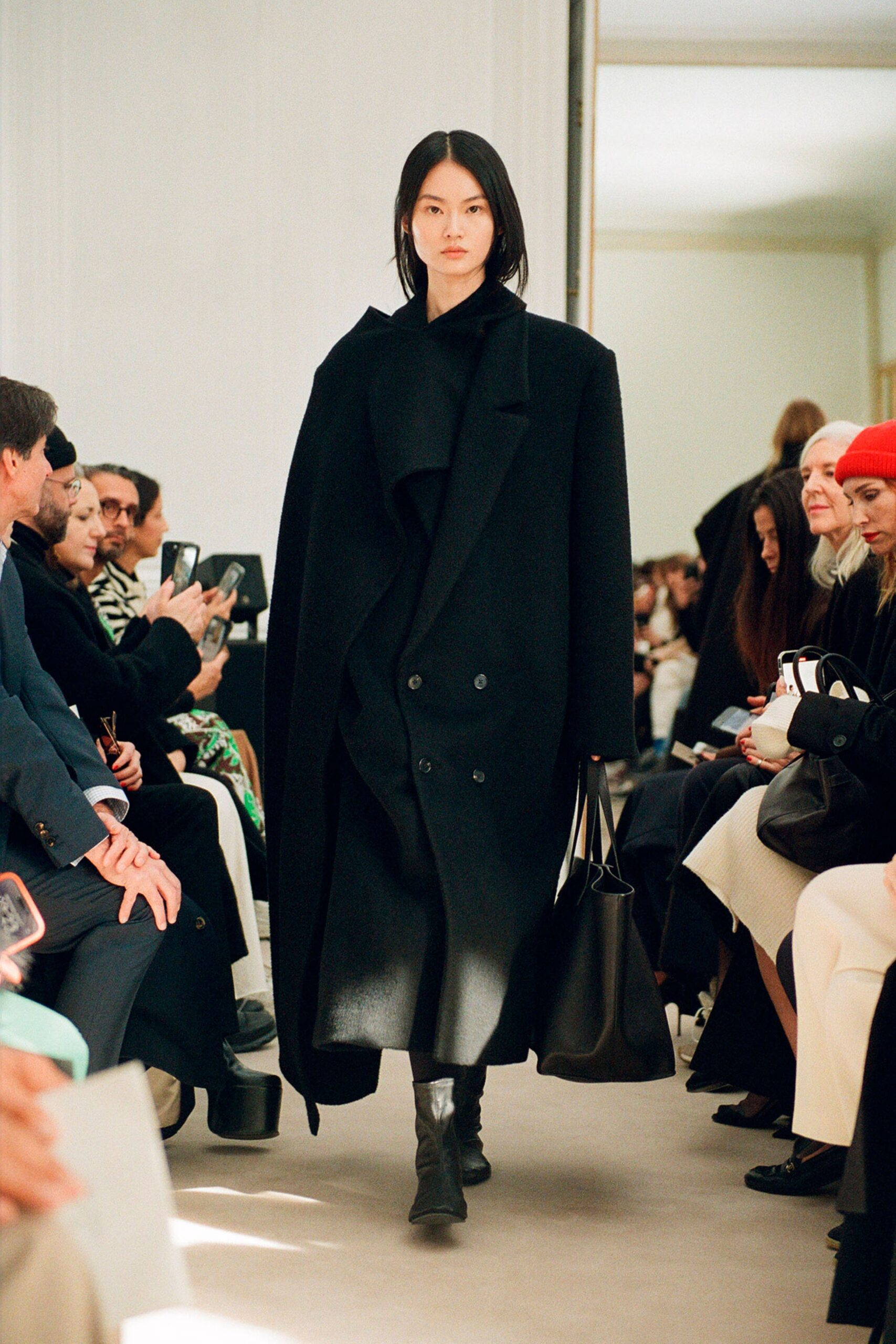 An oversized black wool coat with long sleeves and a collared design featuring button details.