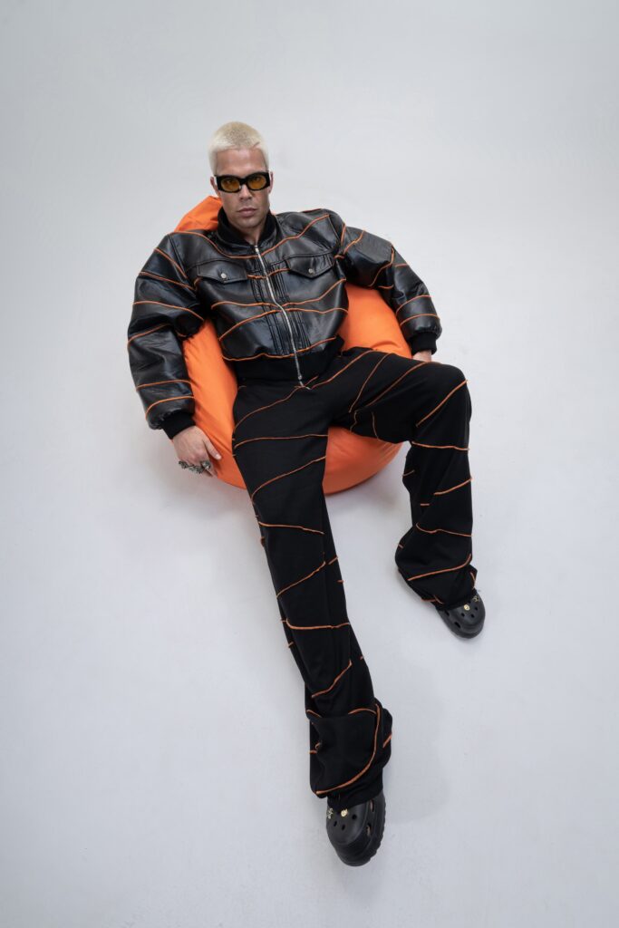 A relaxed black leather jacket with orange detailing paired with printed pants.