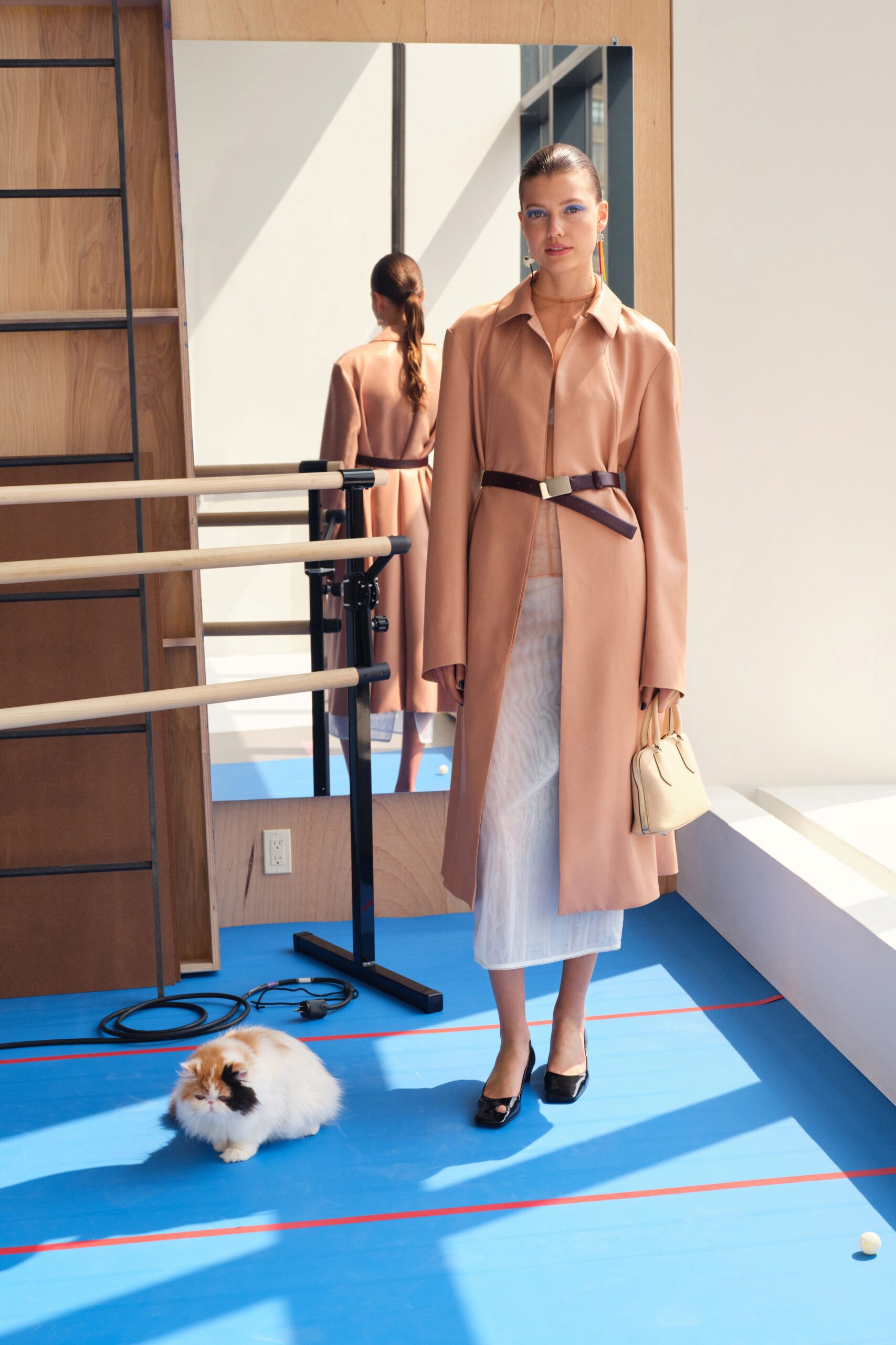 A fitted beige leather coat paired with a white silk skirt, featuring a belted design and long sleeves.