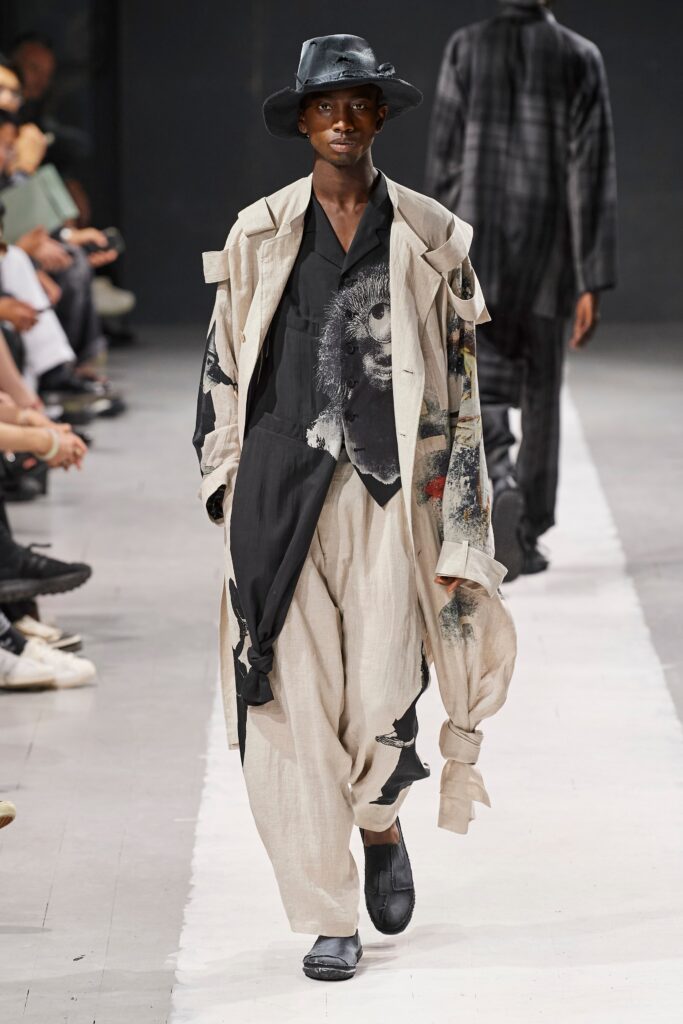 A relaxed-fit beige coat paired with black pants, featuring a layered design and long sleeves.