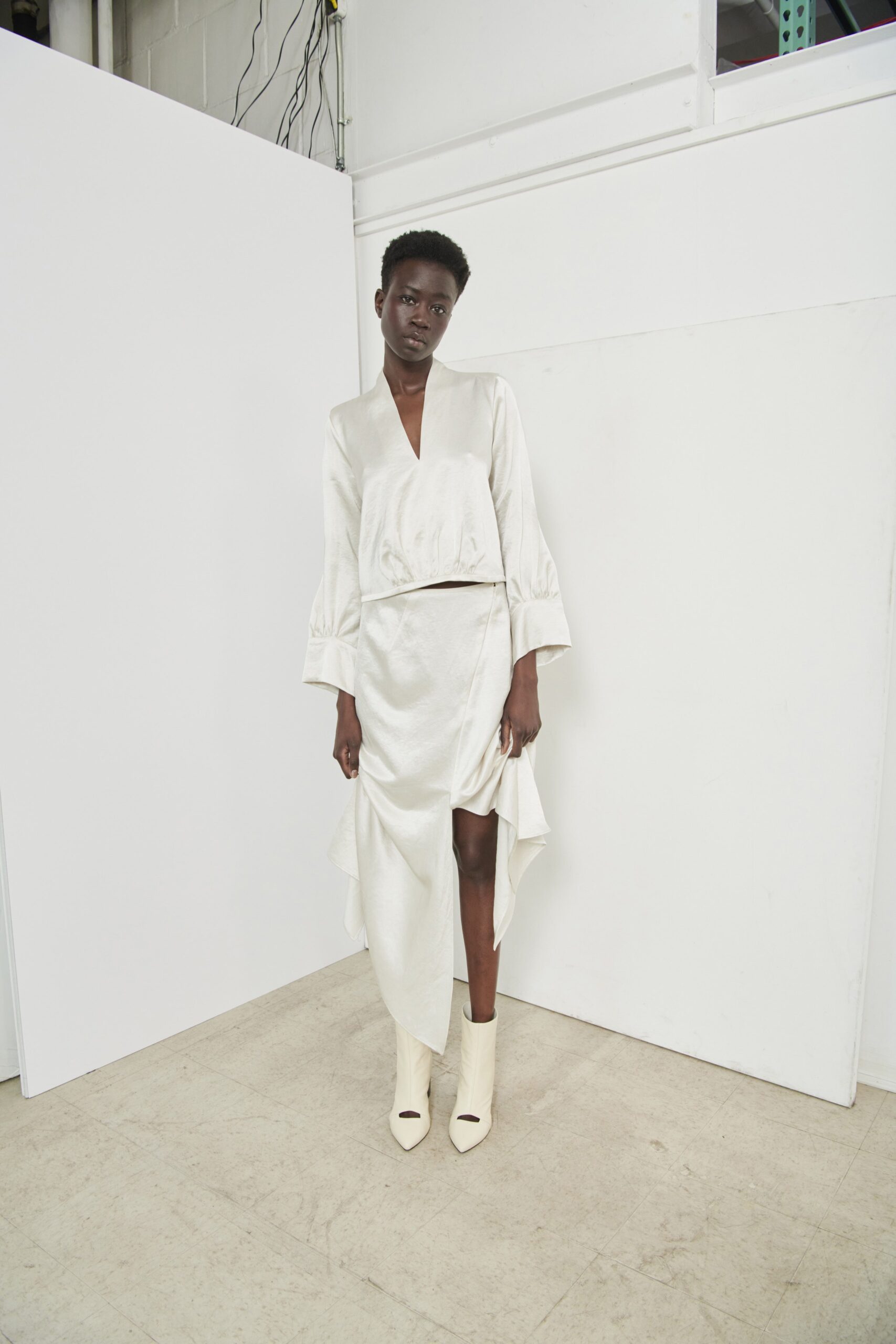 A fitted white silk dress with long sleeves, a V-neckline, and an asymmetric ruffled hem.