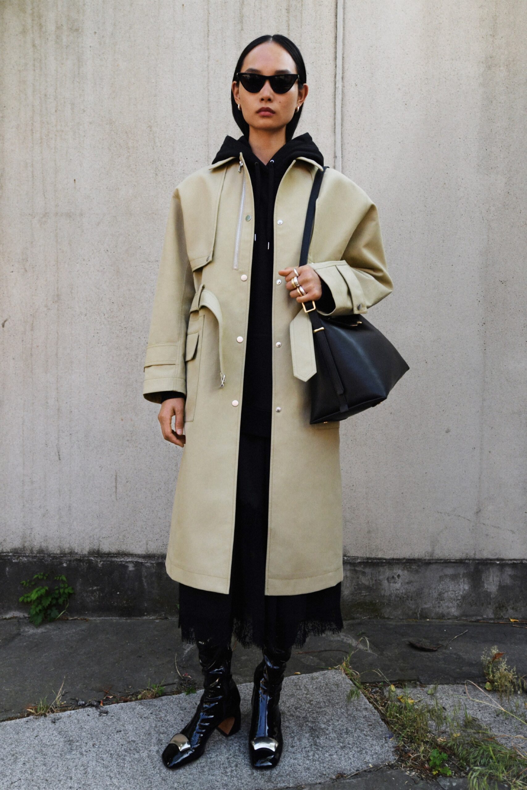 A relaxed beige coat layered over a black dress with long sleeves and a hood.