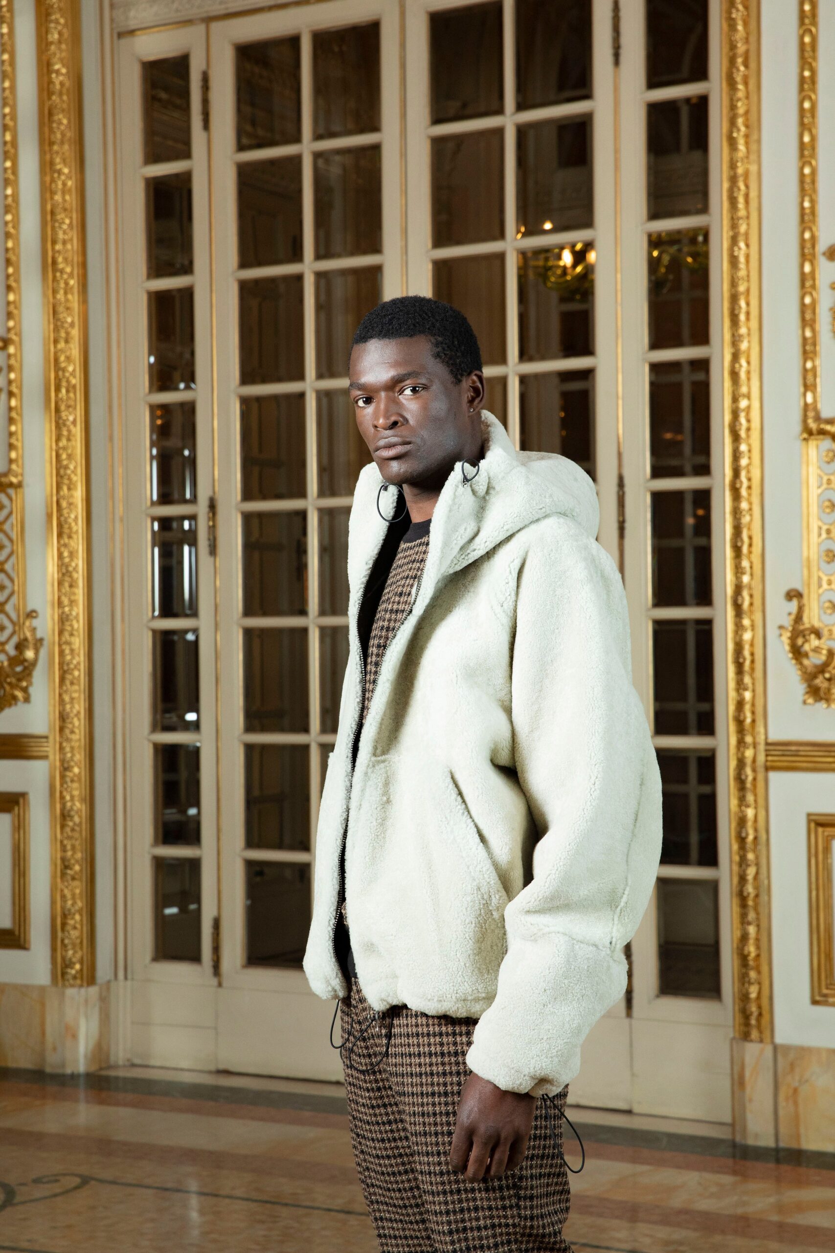 A relaxed cream faux-fur hooded jacket paired with checked brown pants.