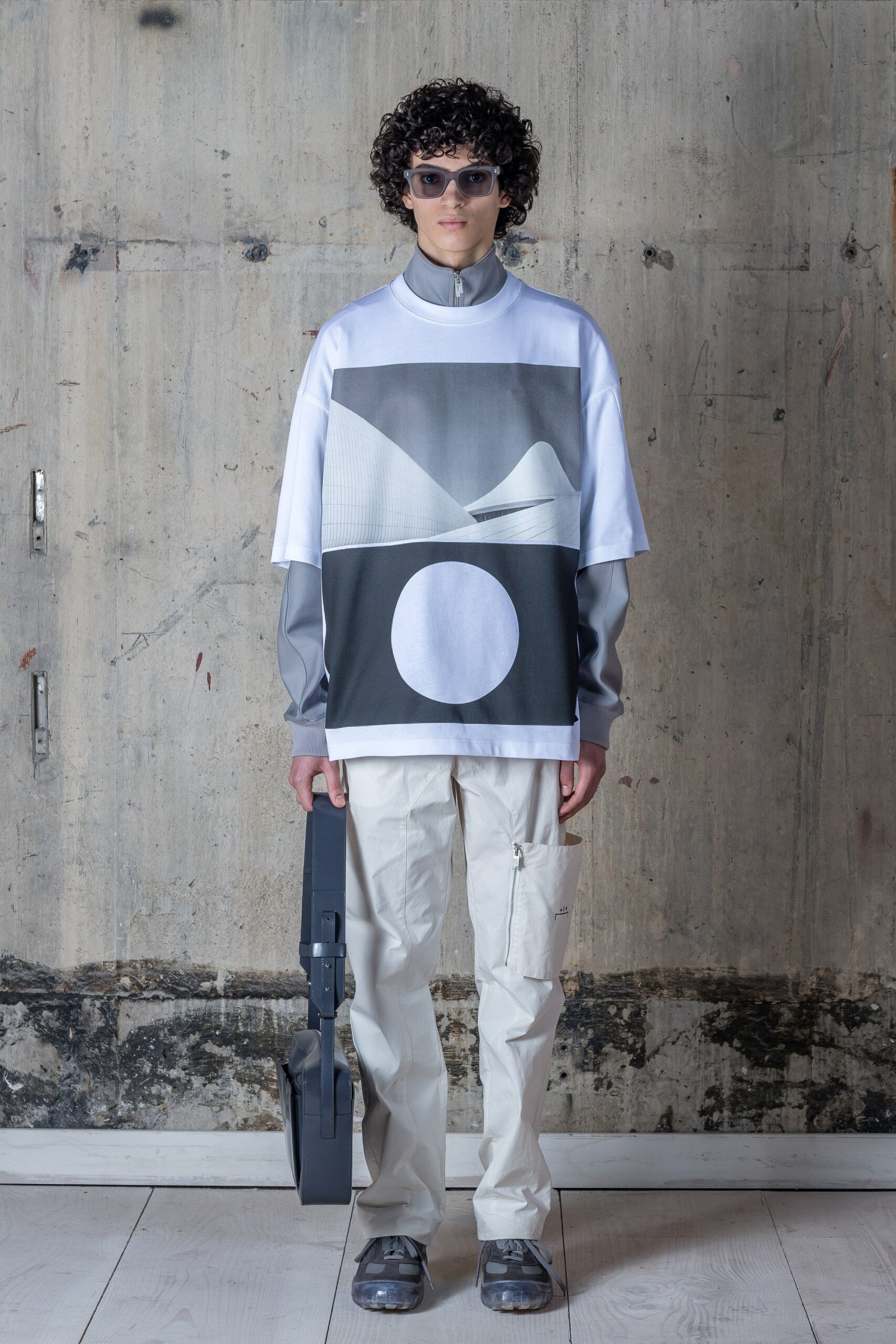 A relaxed white long-sleeve top with a printed design paired with gray pants.