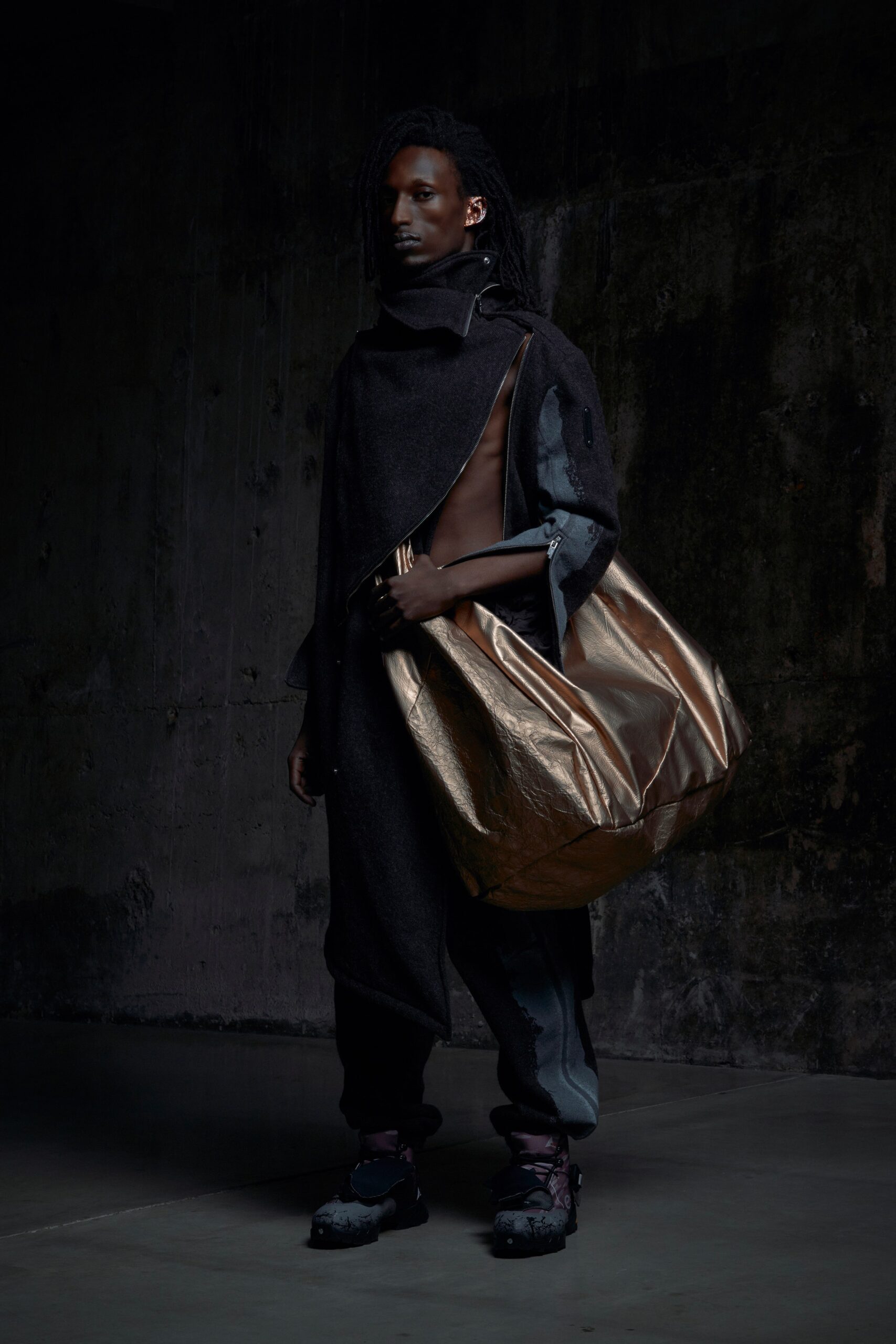 A relaxed black wool cape paired with gray pants, featuring an asymmetric design and a unique silhouette.