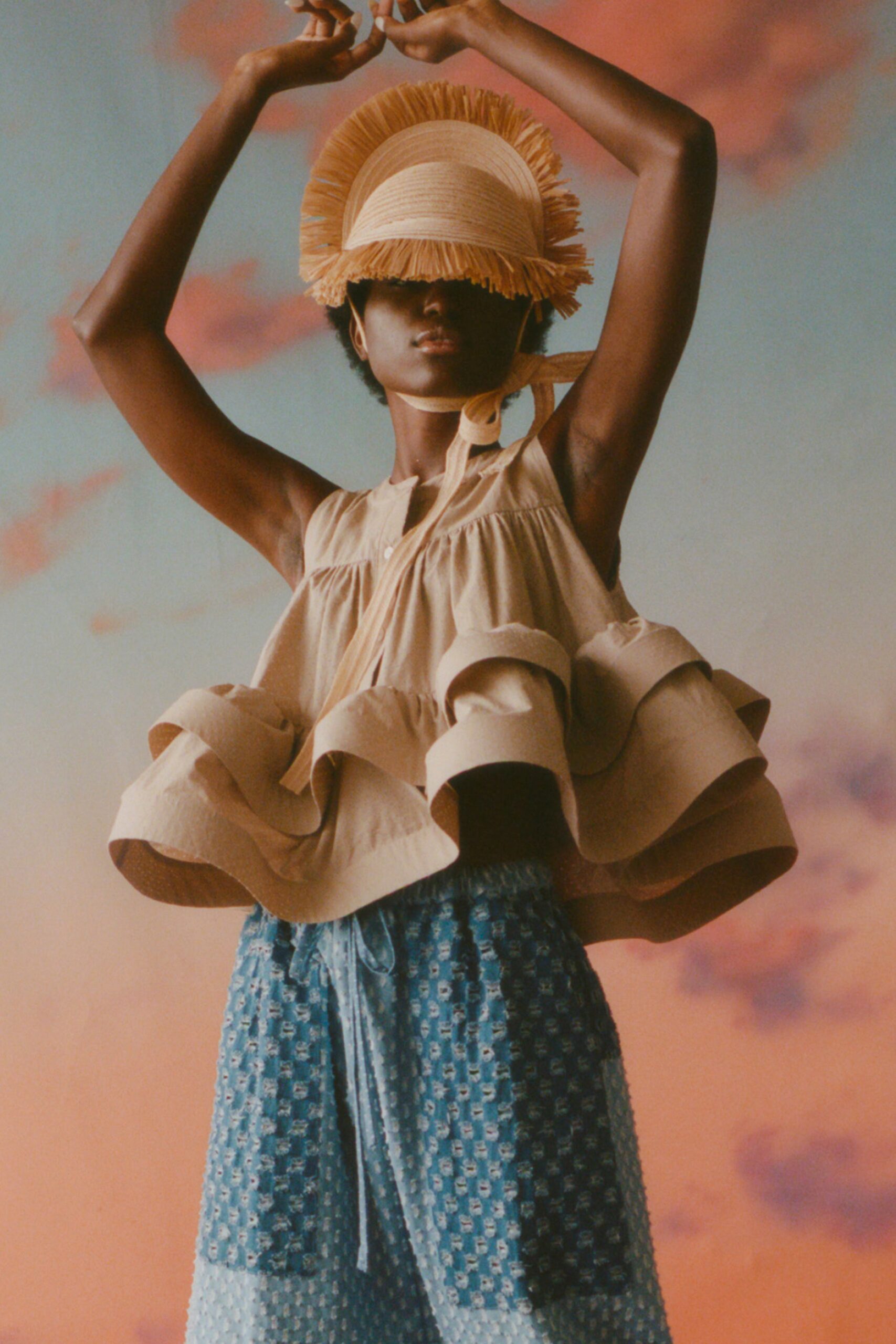 This relaxed sleeveless top features playful ruffles that create a dynamic silhouette, complemented by a collared neckline. Paired with printed blue pants, the ensemble showcases a harmonious blend of textures and colors, evoking a sense of effortless style.