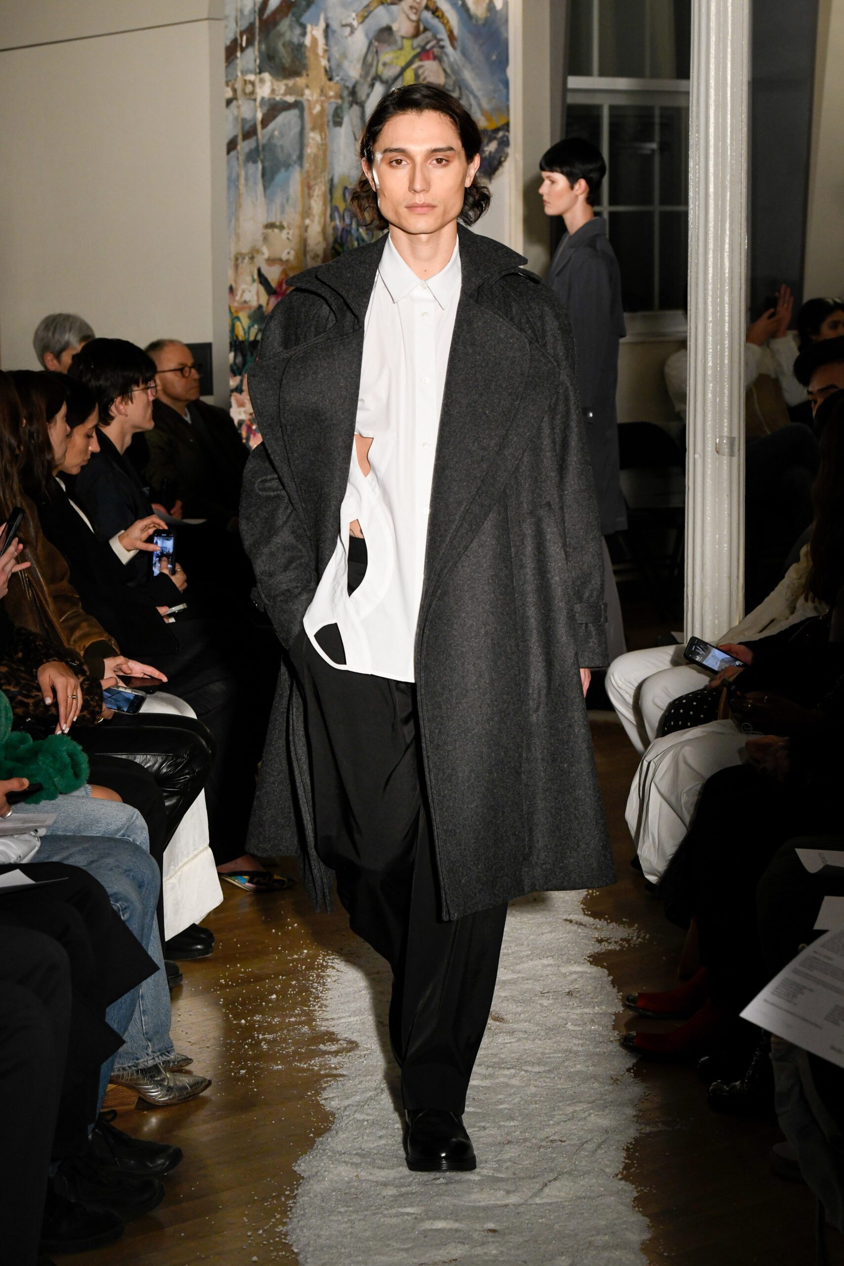 A relaxed black wool coat layered over a collared white cotton shirt.