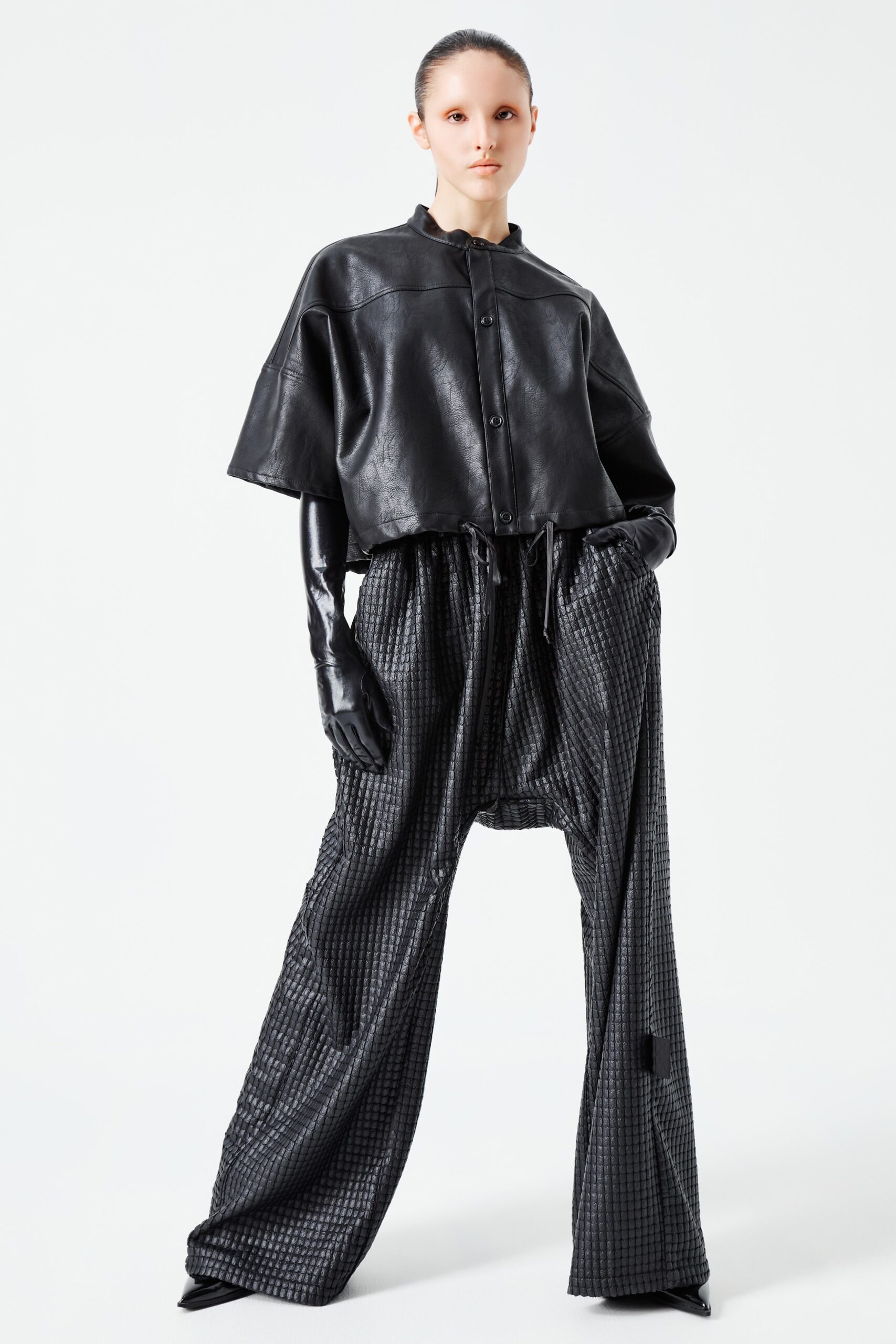 This ensemble features a relaxed black leather top with a collared neckline and short sleeves, paired with wide-leg pants that create a striking silhouette. The combination of structured and flowing elements offers a contemporary take on modern streetwear, emphasizing both comfort and style.