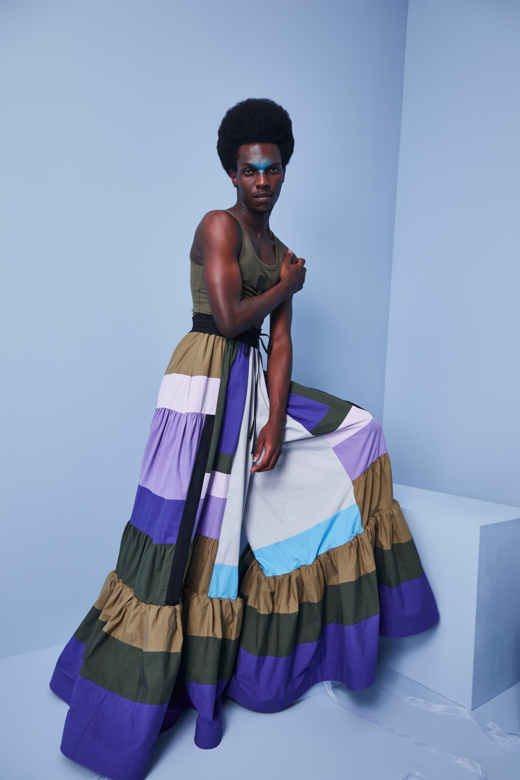 This relaxed sleeveless dress features a striking color-blocked design with tiers that create a sense of movement. The combination of purple, green, and blue panels adds a playful yet sophisticated touch, while the V-neckline enhances the overall silhouette.