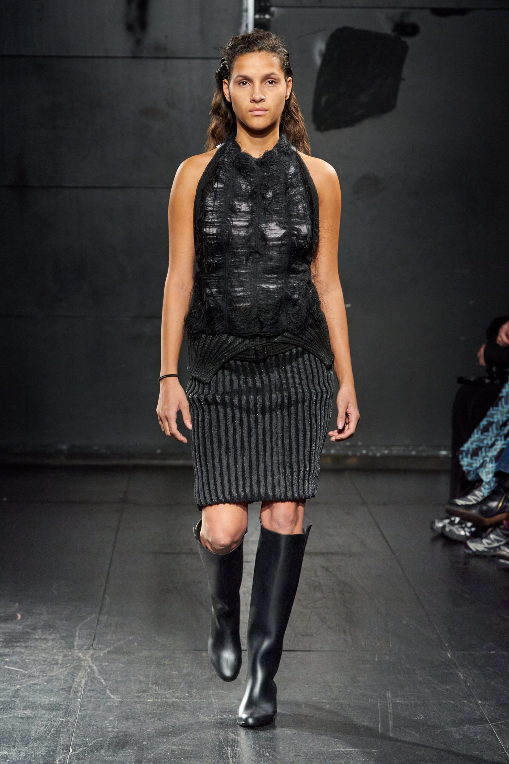 A fitted black sleeveless top with a high neck paired with a striped skirt.