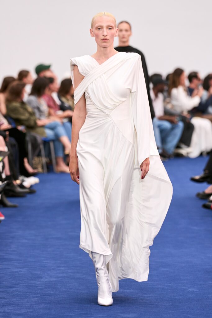 A fitted white silk sleeveless dress with a high neckline and asymmetric design.