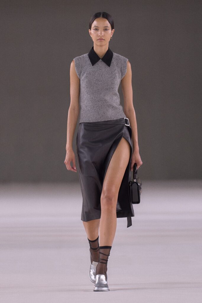 A fitted gray sleeveless top with a collared neckline paired with a black leather asymmetric skirt featuring a slit.