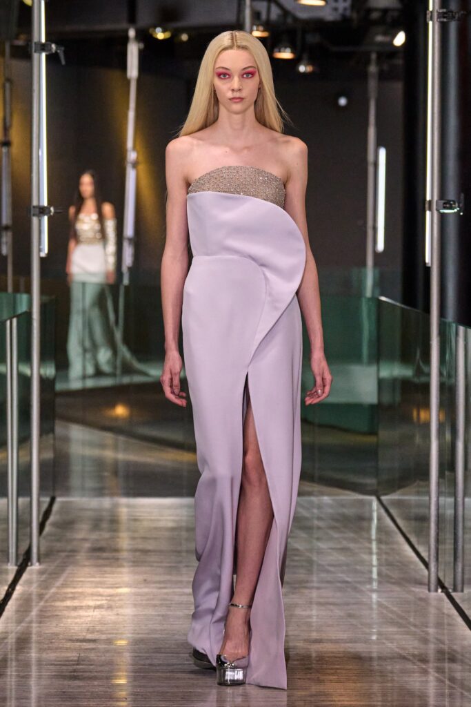 A fitted lavender silk gown with a sleeveless design, high-neck, and a draped silhouette featuring a slit.