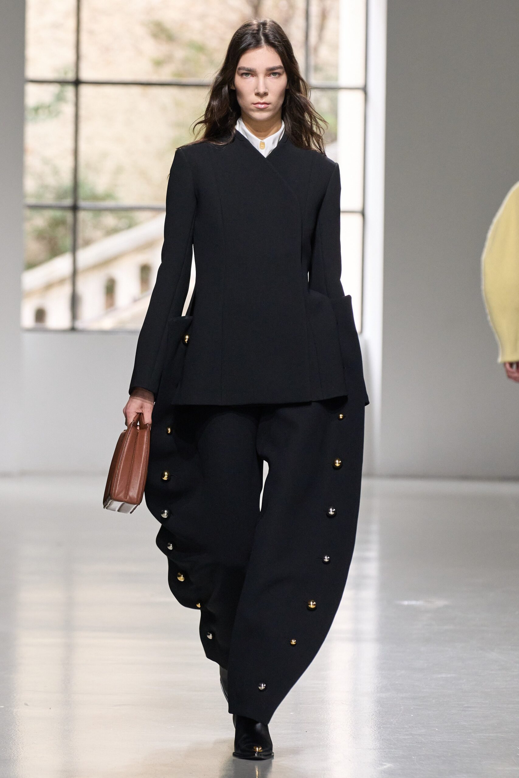 A fitted black wool jacket with long sleeves and asymmetric pants featuring button details.