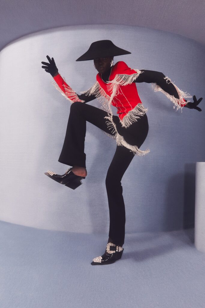 A fitted red top with fringed details paired with black fitted pants.