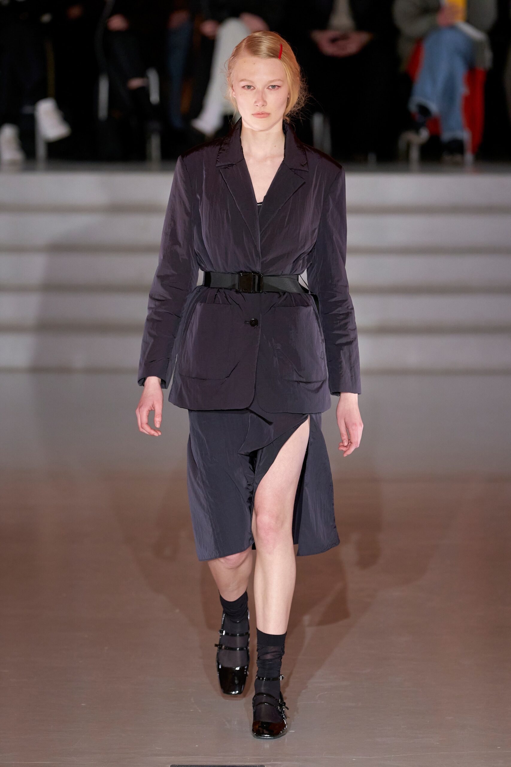 A fitted black dress with an asymmetric slit, layered under a matching jacket.
