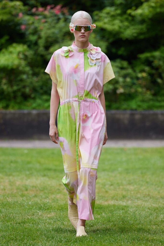 A short-sleeve belted jumpsuit in pink with green and yellow floral patterns.