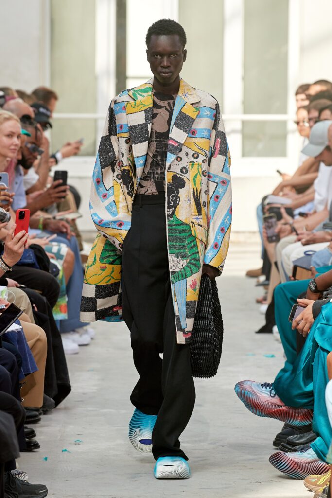 A relaxed fit multicolor printed coat paired with black pants, showcasing a unique artistic design.