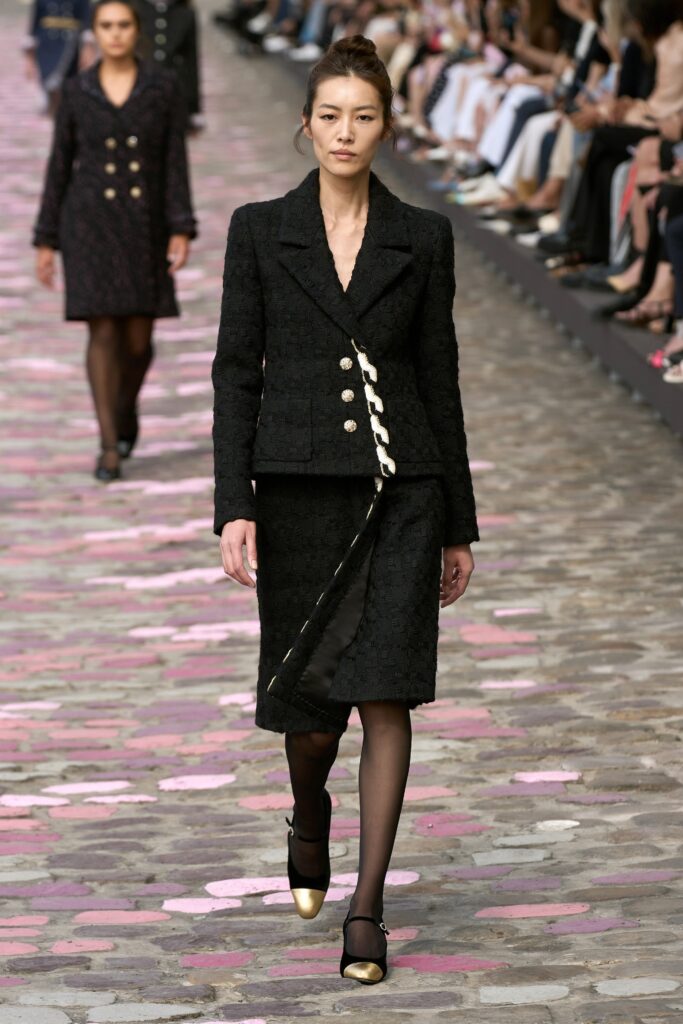 A fitted black tweed blazer with a collared design and a pencil skirt, featuring button details.