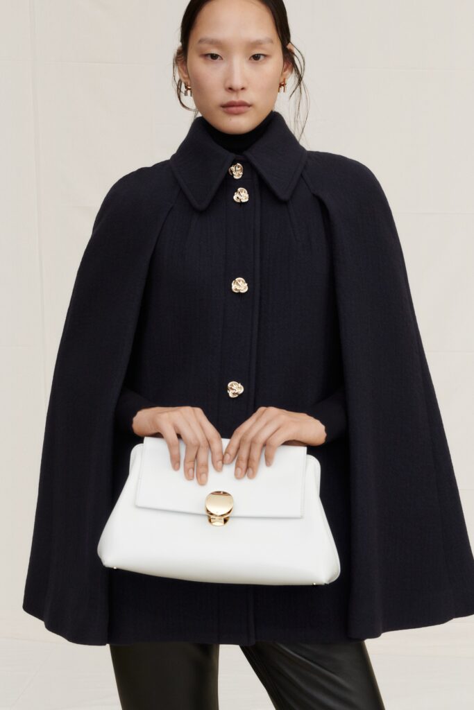 A fitted black wool cape dress with long sleeves and a collared neckline featuring button details.