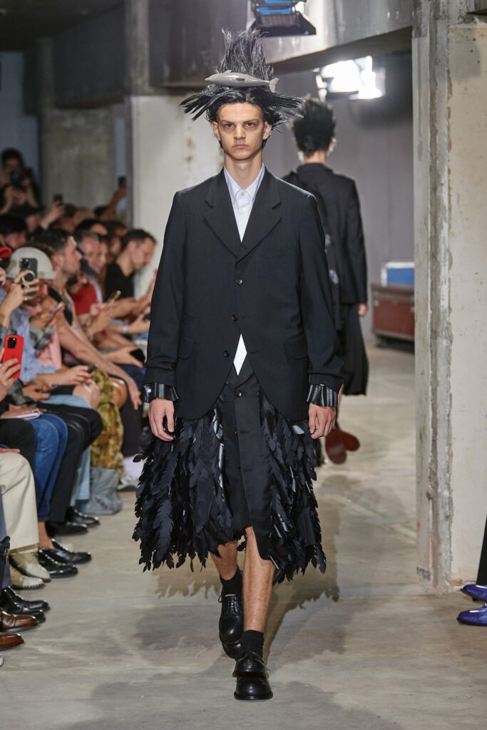 A relaxed black jacket with long sleeves and a collared design, paired with an asymmetric fringed skirt.