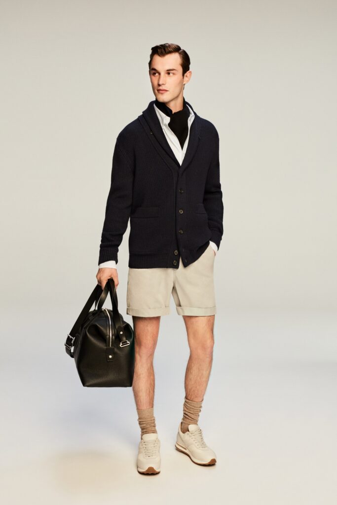 A relaxed navy cardigan with long sleeves, paired with collared shirt and beige shorts.