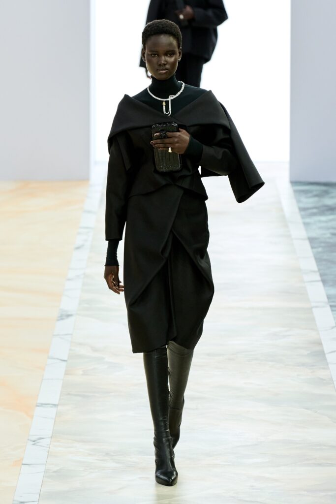 A fitted black dress with long sleeves, a high neckline, and an asymmetric design detail.