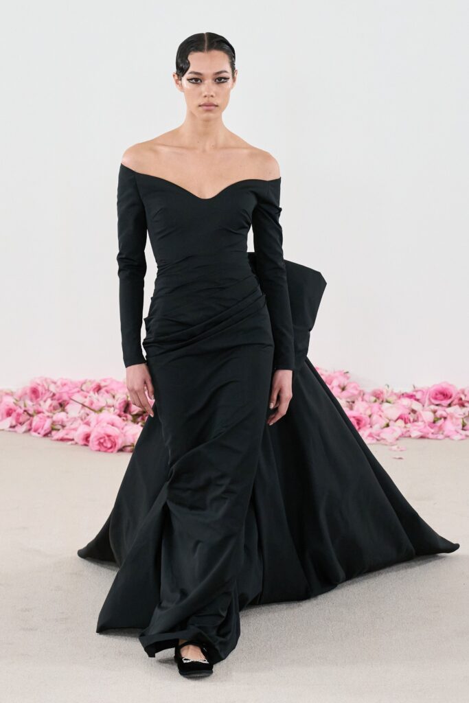 A fitted black silk gown with long sleeves and an off-shoulder design featuring draped detailing.