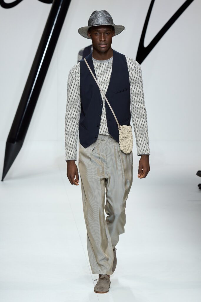A relaxed black vest paired with printed long-sleeve shirt and wide-leg gray pants.