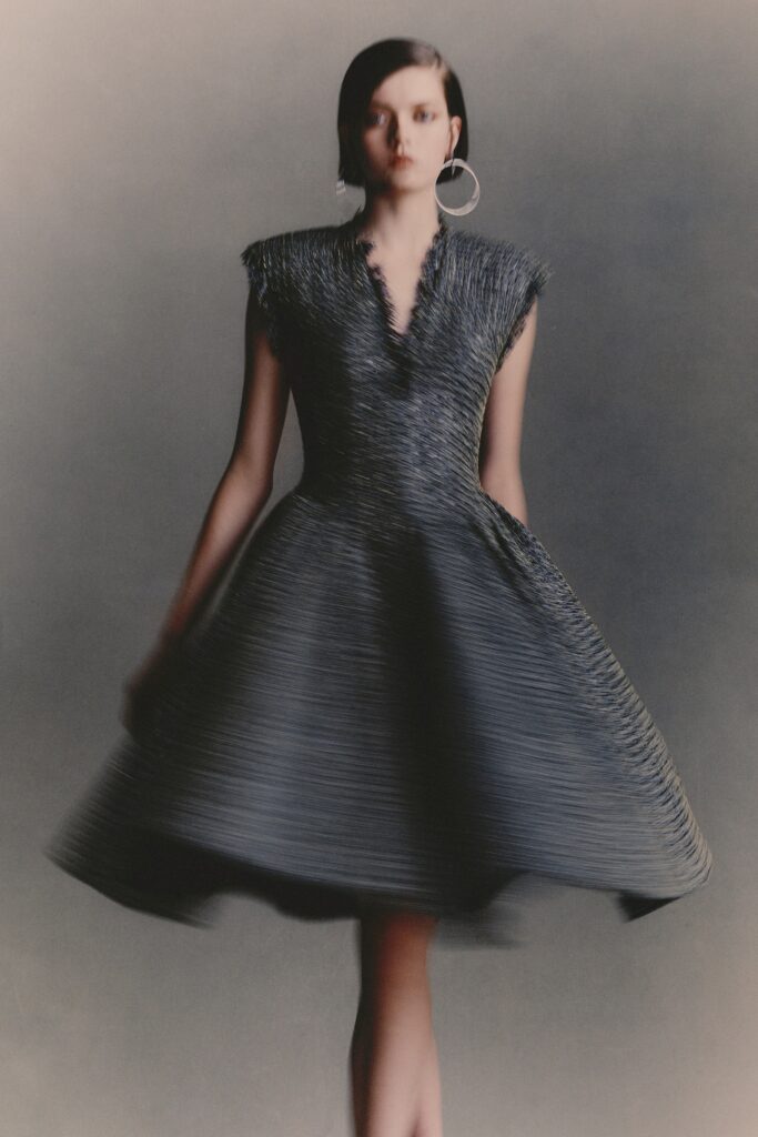 A fitted black silk sleeveless dress with a V-neckline and pleated A-line silhouette.