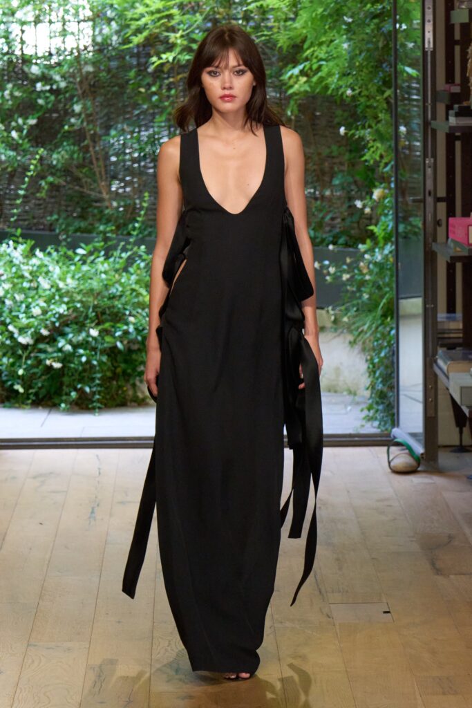 A fitted black silk sleeveless dress with a deep V-neckline and asymmetric design details.