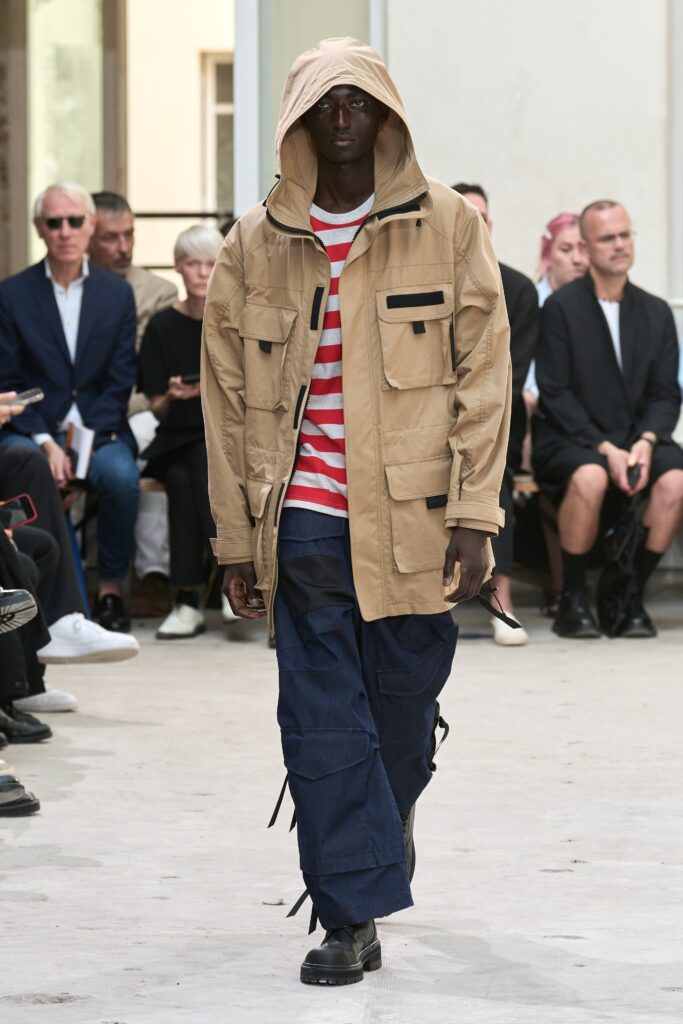 A relaxed beige hooded jacket paired with a striped shirt and blue pants.