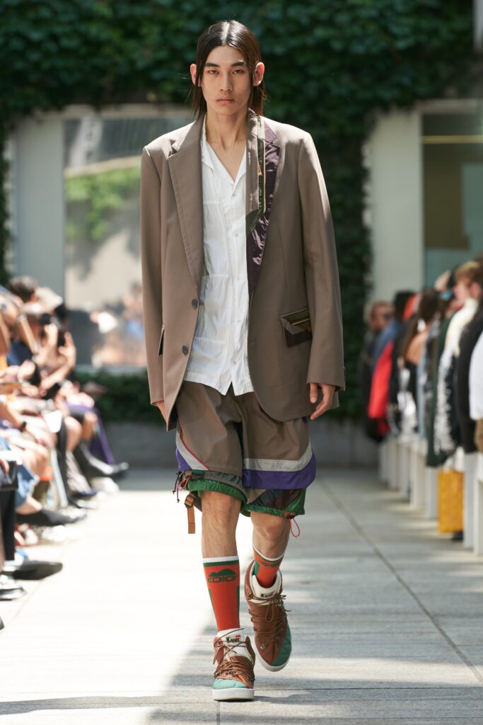 A relaxed brown jacket paired with white collared shirt and layered shorts.