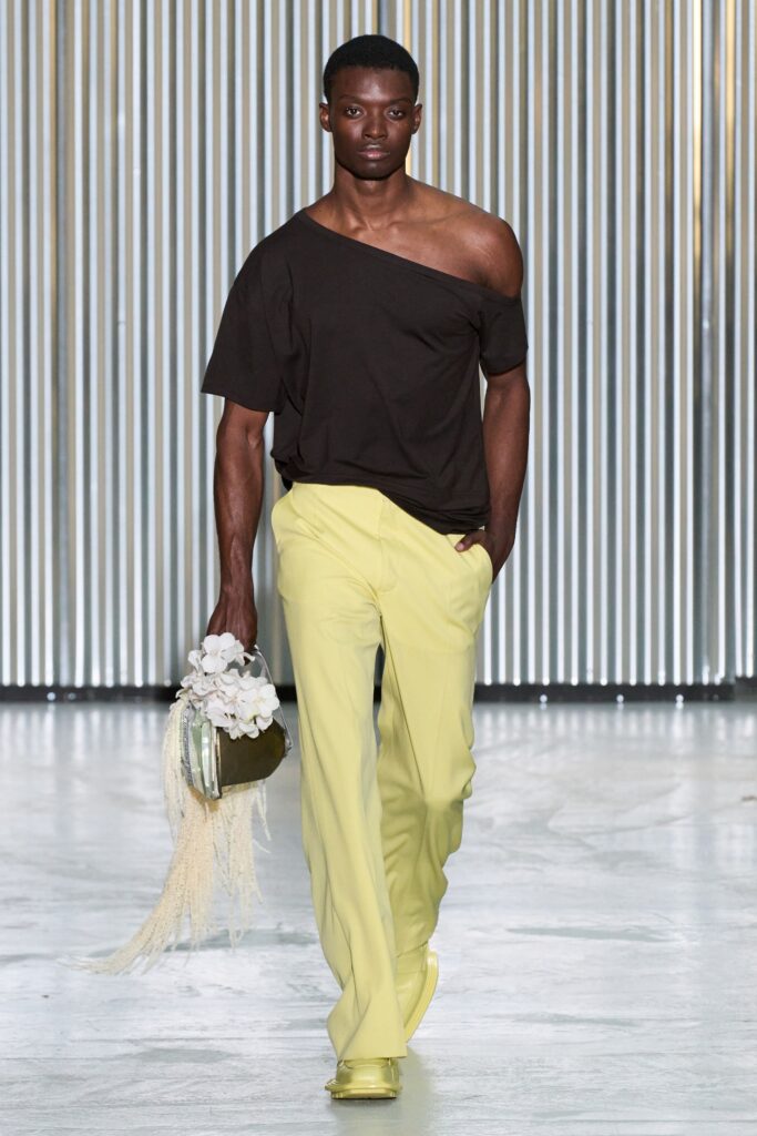 A relaxed black off-shoulder top paired with straight-leg yellow pants.