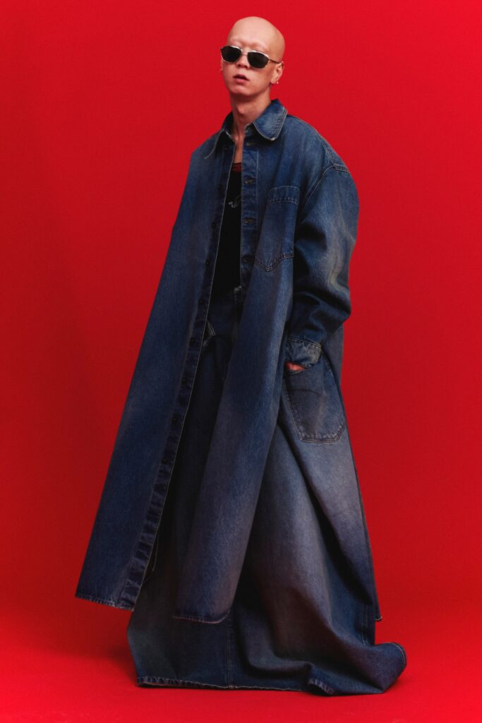 An oversized blue denim coat dress with long sleeves and an asymmetric layered design.