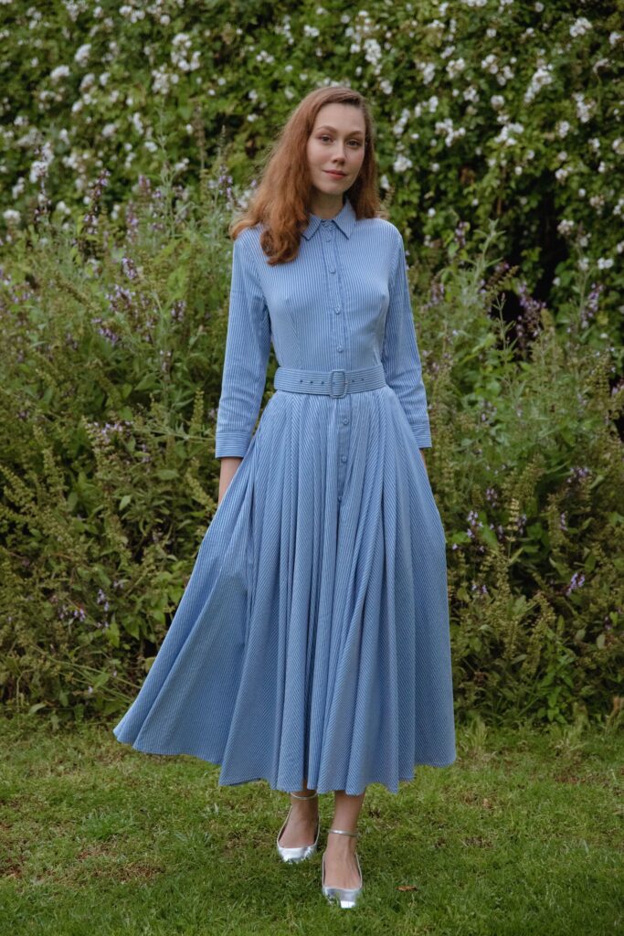 A fitted blue cotton long-sleeve dress with pleats and a belted waist.