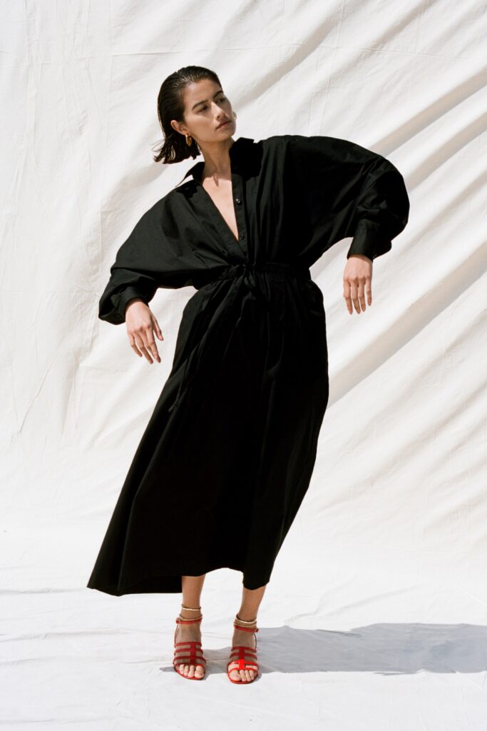 A relaxed black cotton dress with long sleeves and a V-neckline featuring a tiered design.