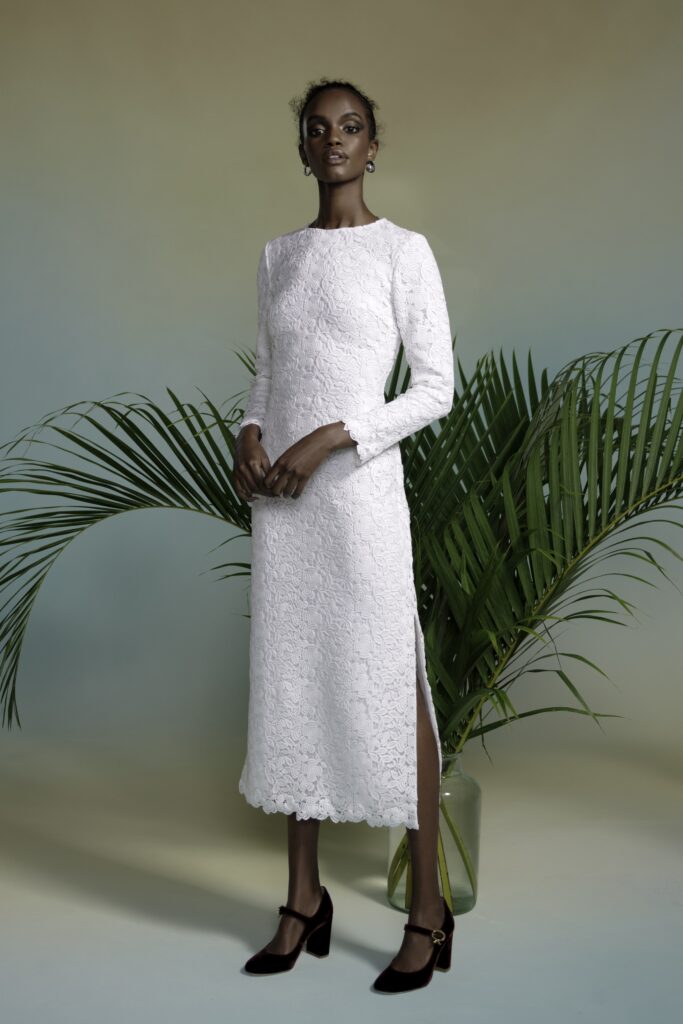 A fitted white lace dress with long sleeves, a high neckline, and a side slit.