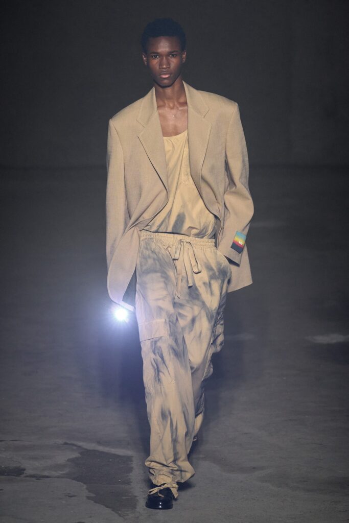 A relaxed beige jacket paired with printed gray pants for a contemporary runway look.