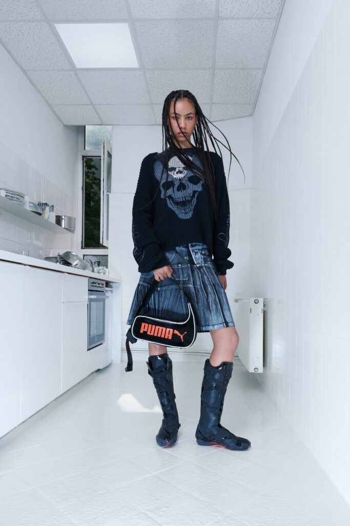 A fitted black pleated denim skirt paired with a long-sleeve top featuring a skull design.