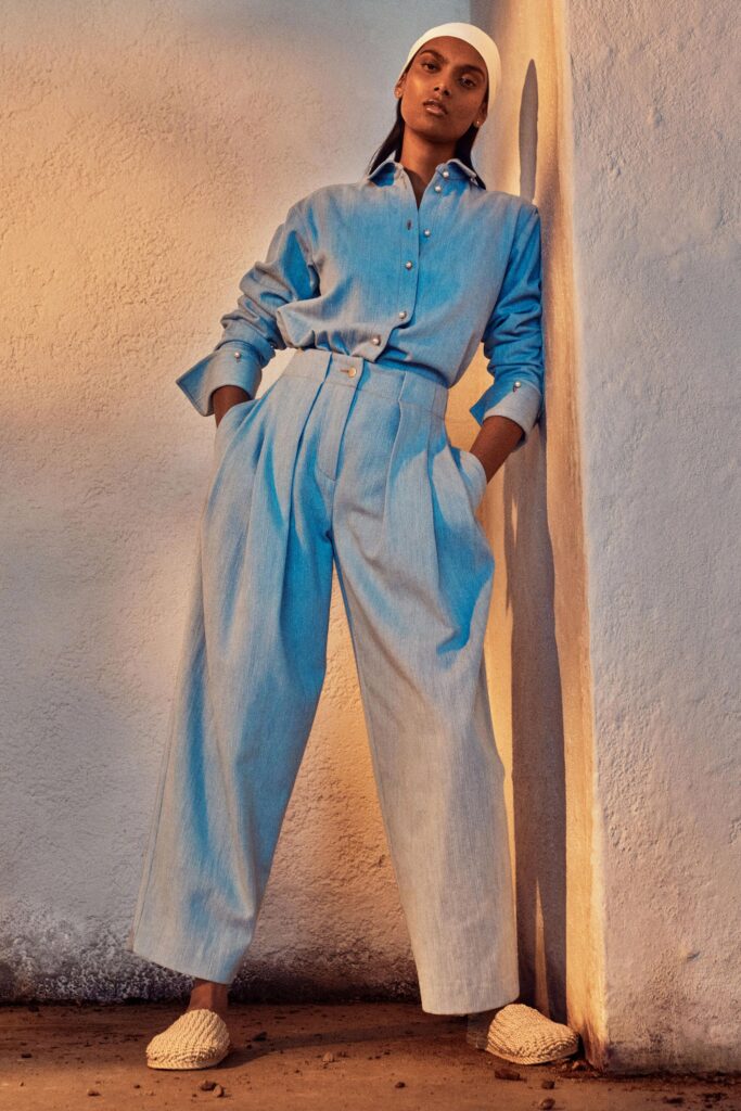 A relaxed blue cotton shirt with long sleeves and collared design paired with pleated wide-leg pants.