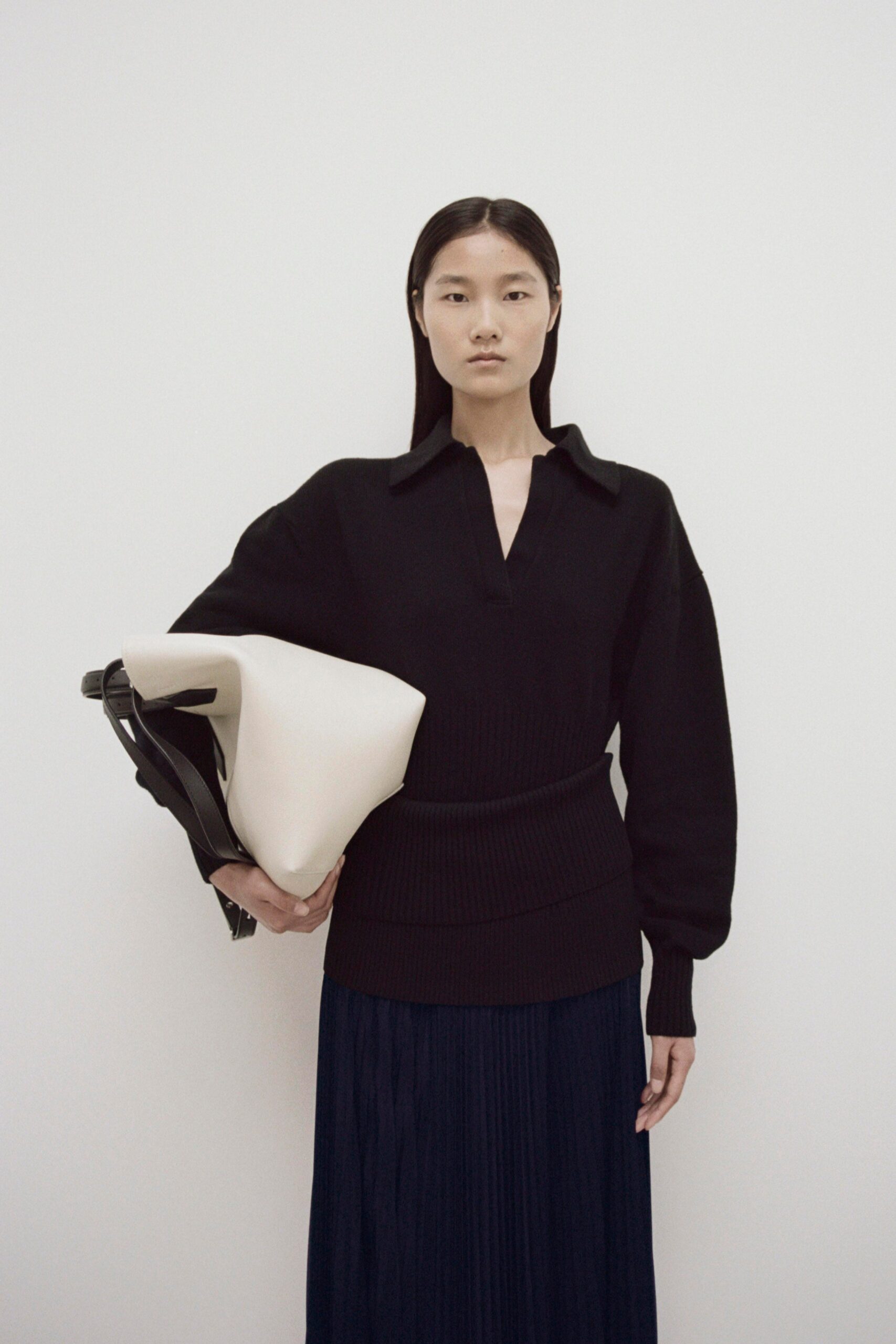 A relaxed black top with long sleeves and a collared neckline paired with a pleated navy skirt.