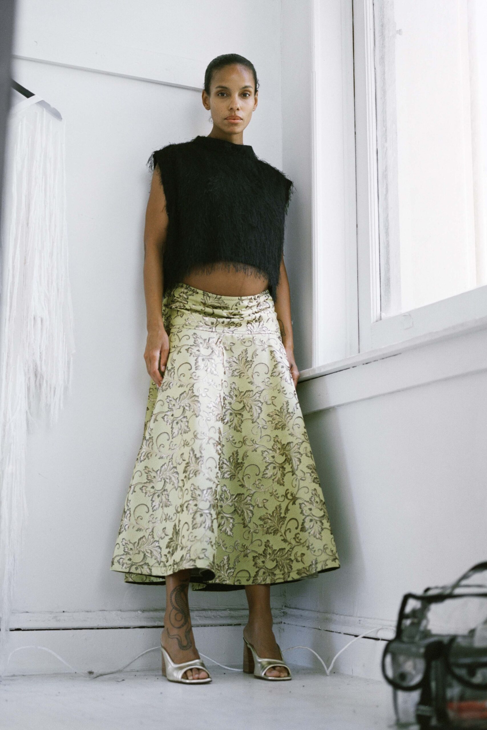 A relaxed black wool sleeveless top paired with a pleated printed skirt.