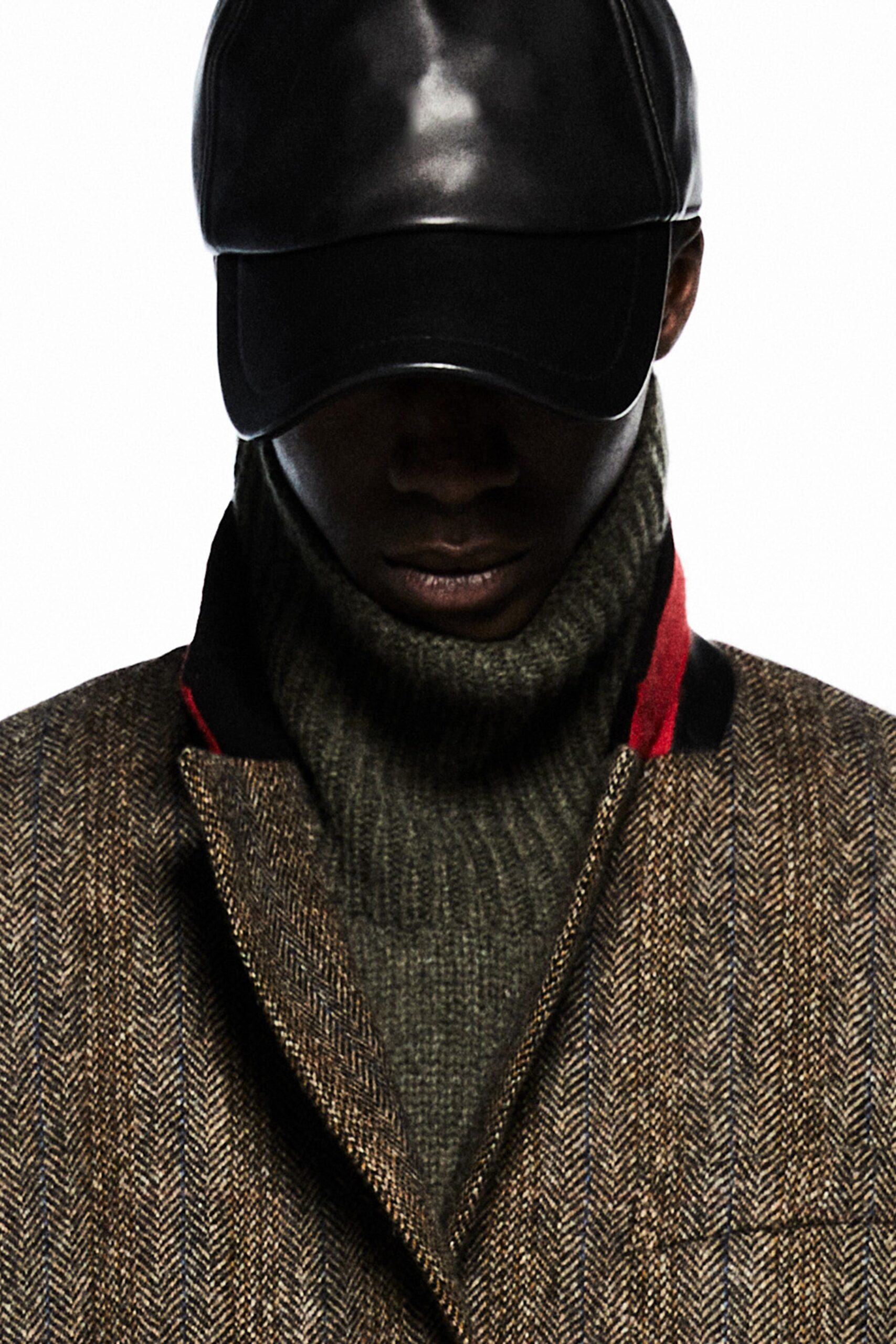 A fitted brown wool coat layered over a gray high-neck sweater, complemented by a black leather cap.